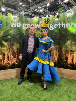 Zwei Personen stehen lächelnd vor einem tropischen Hintergrund mit dem Schriftzug „we grow together“ – ein Symbol für internationale Partnerschaft im Fruchthandel
